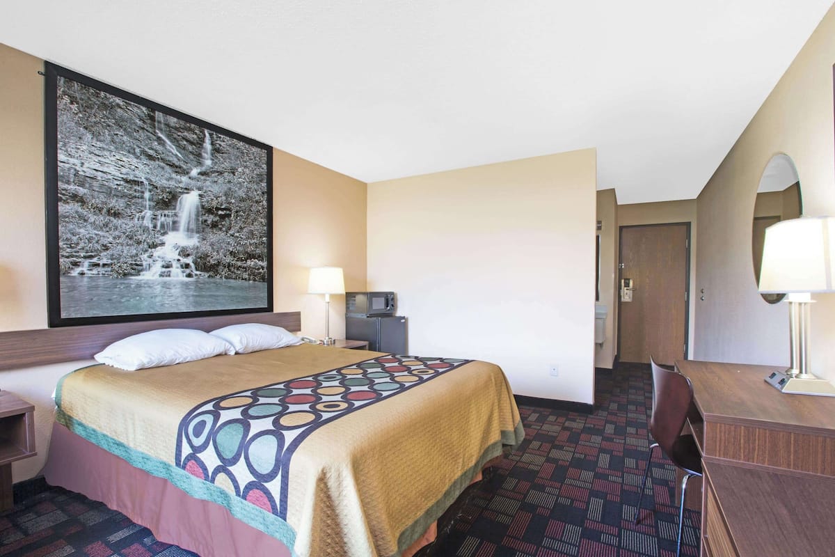 A hotel room with a bed, a desk, a chair, a TV, and a large framed picture of a waterfall.