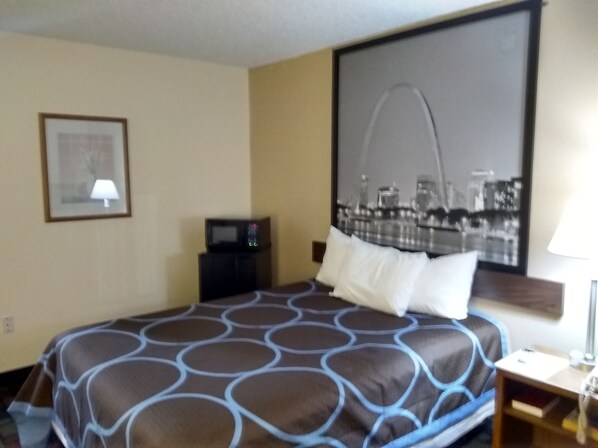 A hotel room with a large bed, a cityscape painting on the wall, a framed picture, and a small table with a lamp. - Super 8 by Wyndham Boonville (Boonville)