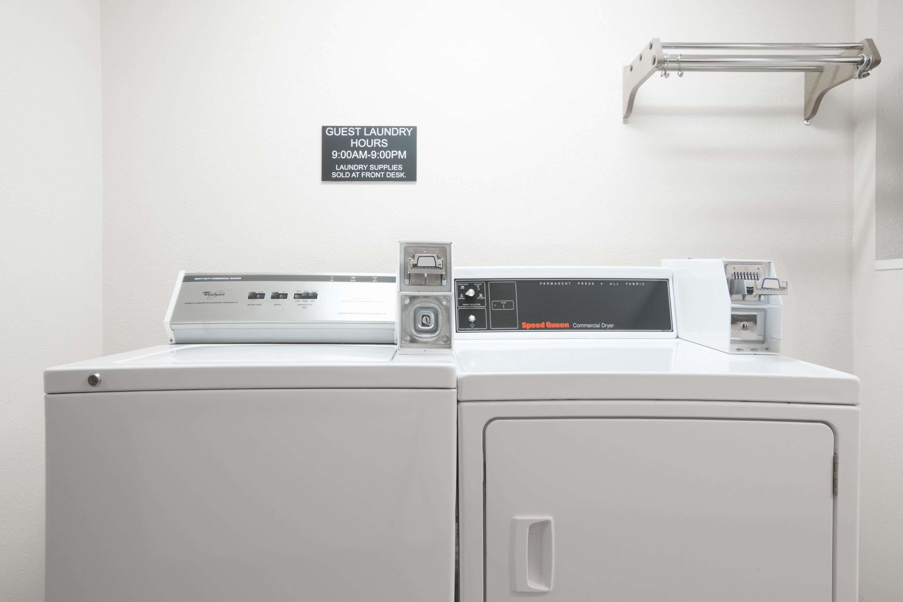 A front-loading washing machine with a Speed Queen commercial dryer, a guest laundry sign, and a metal towel rack.