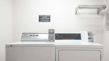 A front-loading washing machine with a Speed Queen commercial dryer, a guest laundry sign, and a metal towel rack.