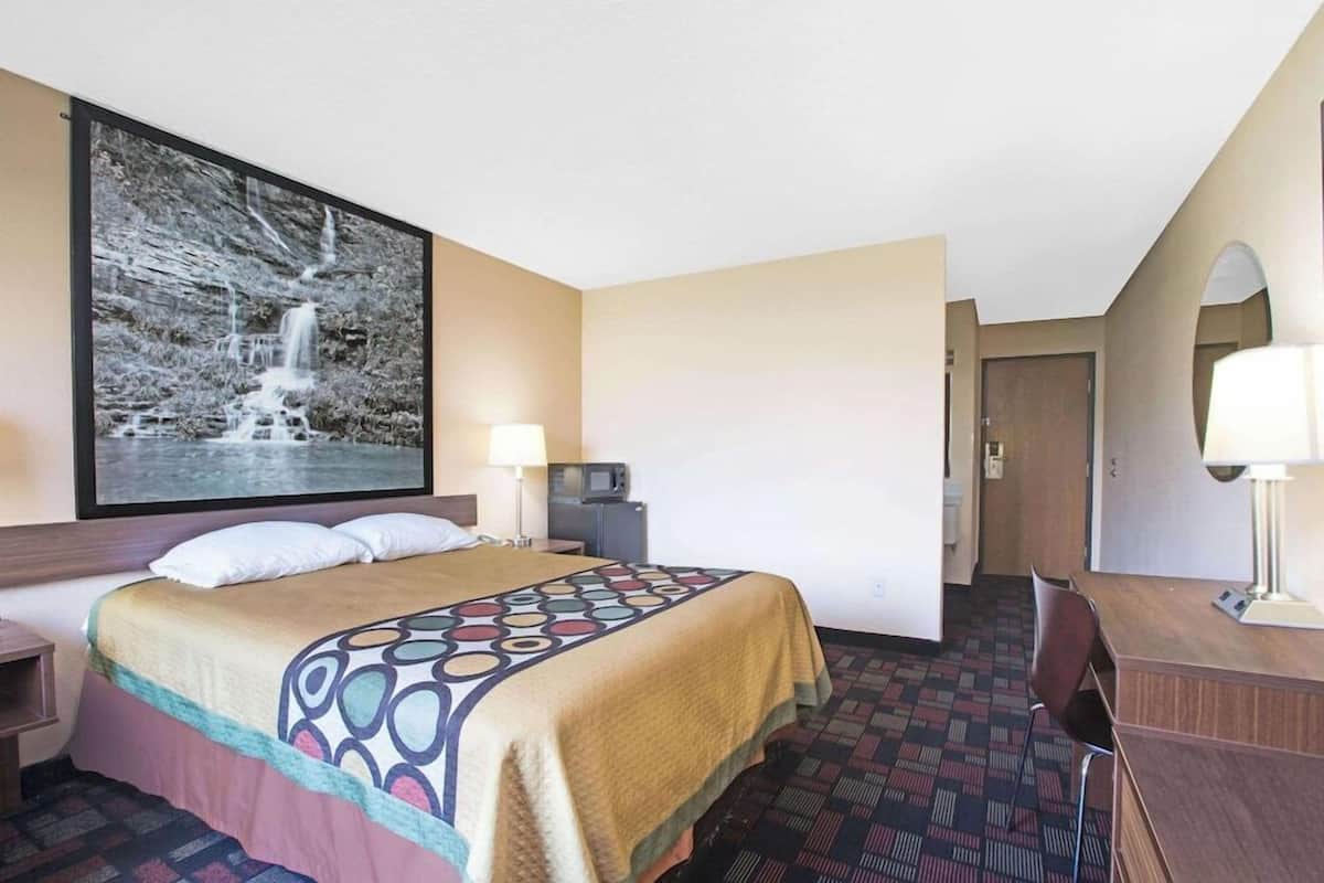 A hotel room with a bed, desk, chair, and a large framed picture of a waterfall.