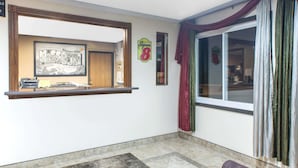 A hotel lobby with a reception desk, a framed welcome sign, and a large window with curtains.