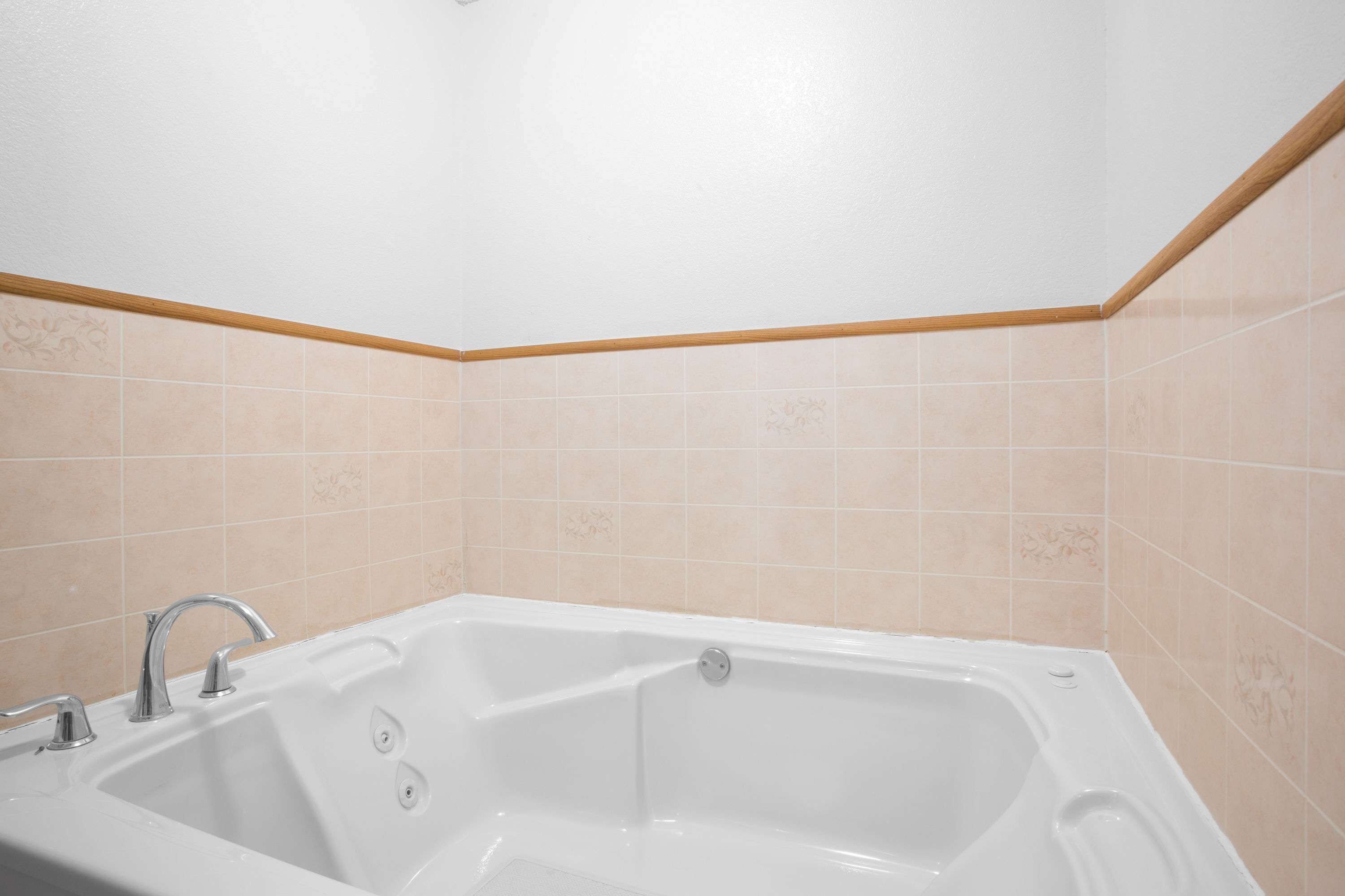 A bathroom with a white bathtub, a double sink, and beige patterned tiles on the walls.