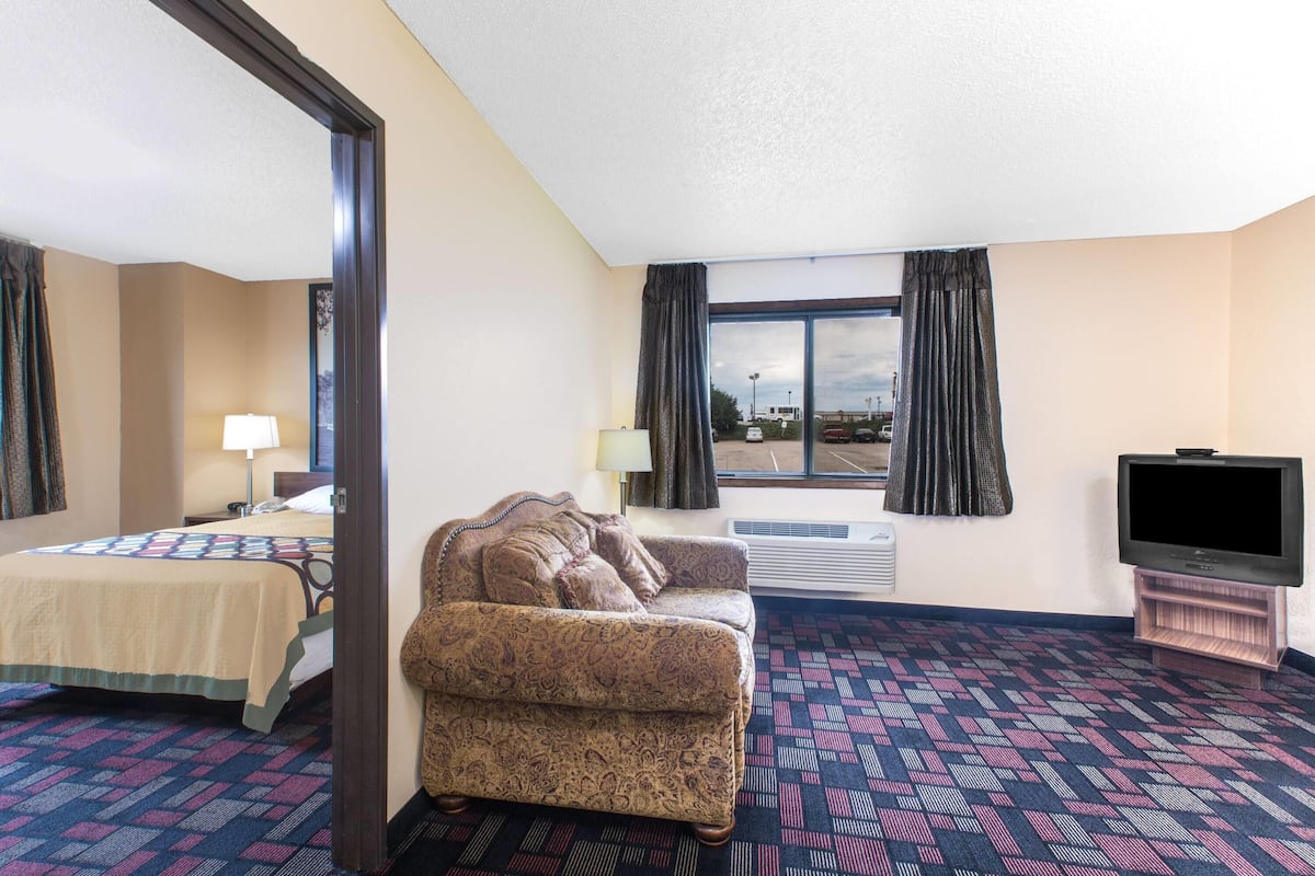 A hotel room with a bed, a sofa, a television, and a large window with curtains.