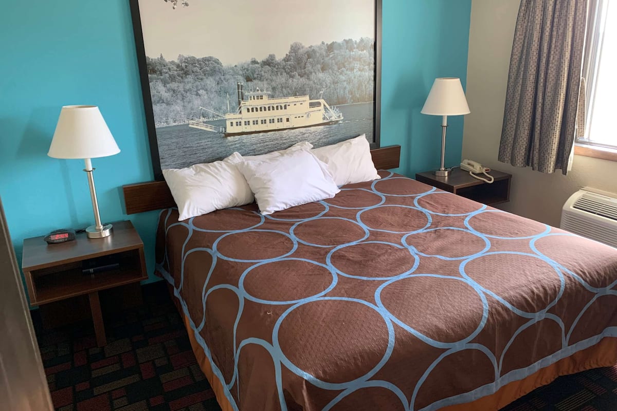 A hotel room with a bed, two bedside tables with lamps, a clock, and a painting of a boat on water.