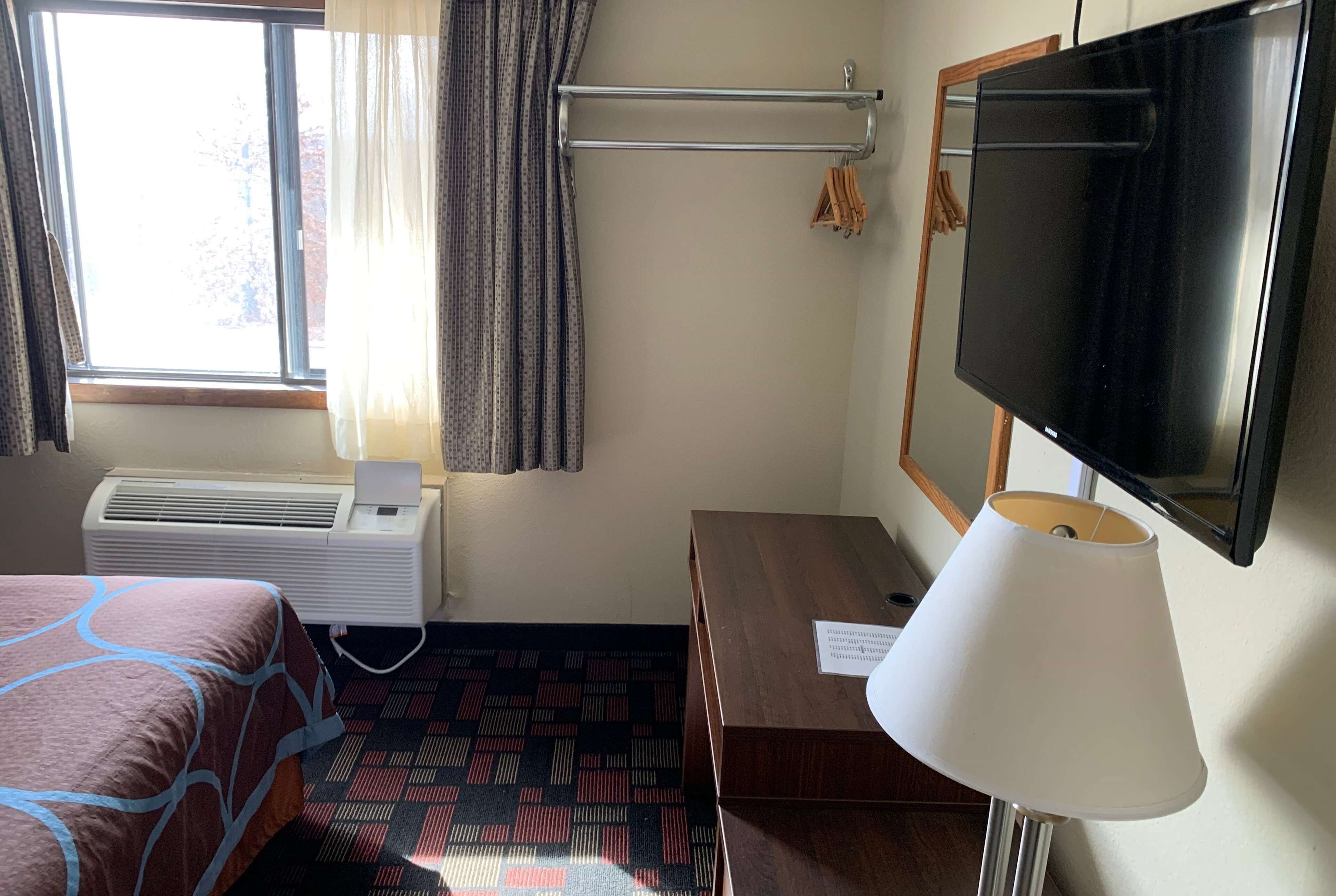 Habitación de hotel con cama, escritorio, televisor, aire acondicionado y ventana con cortinas.