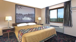 A hotel room with a bed, two bedside tables, a window with curtains, a wall-mounted air conditioner, and a large picture of a boat on the wall.