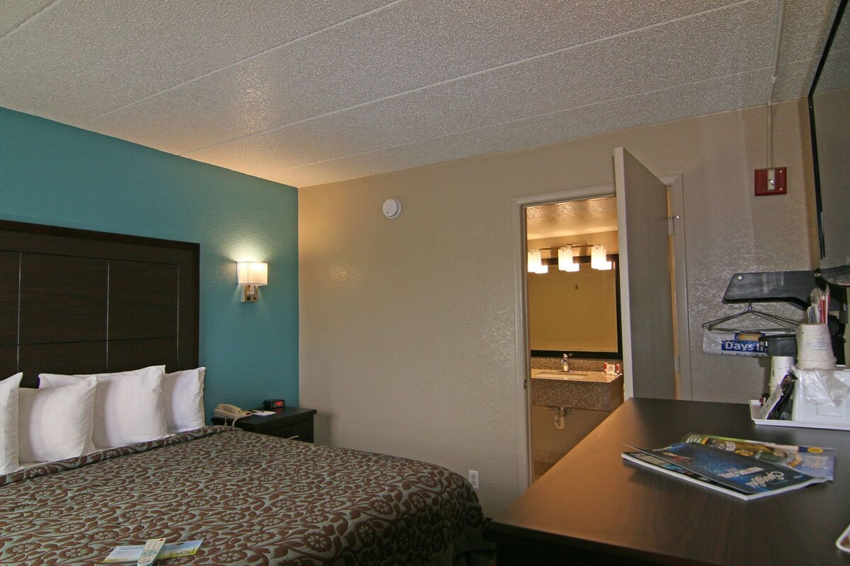 A hotel room with a bed, bedside table, lamp, and a view into the bathroom.
