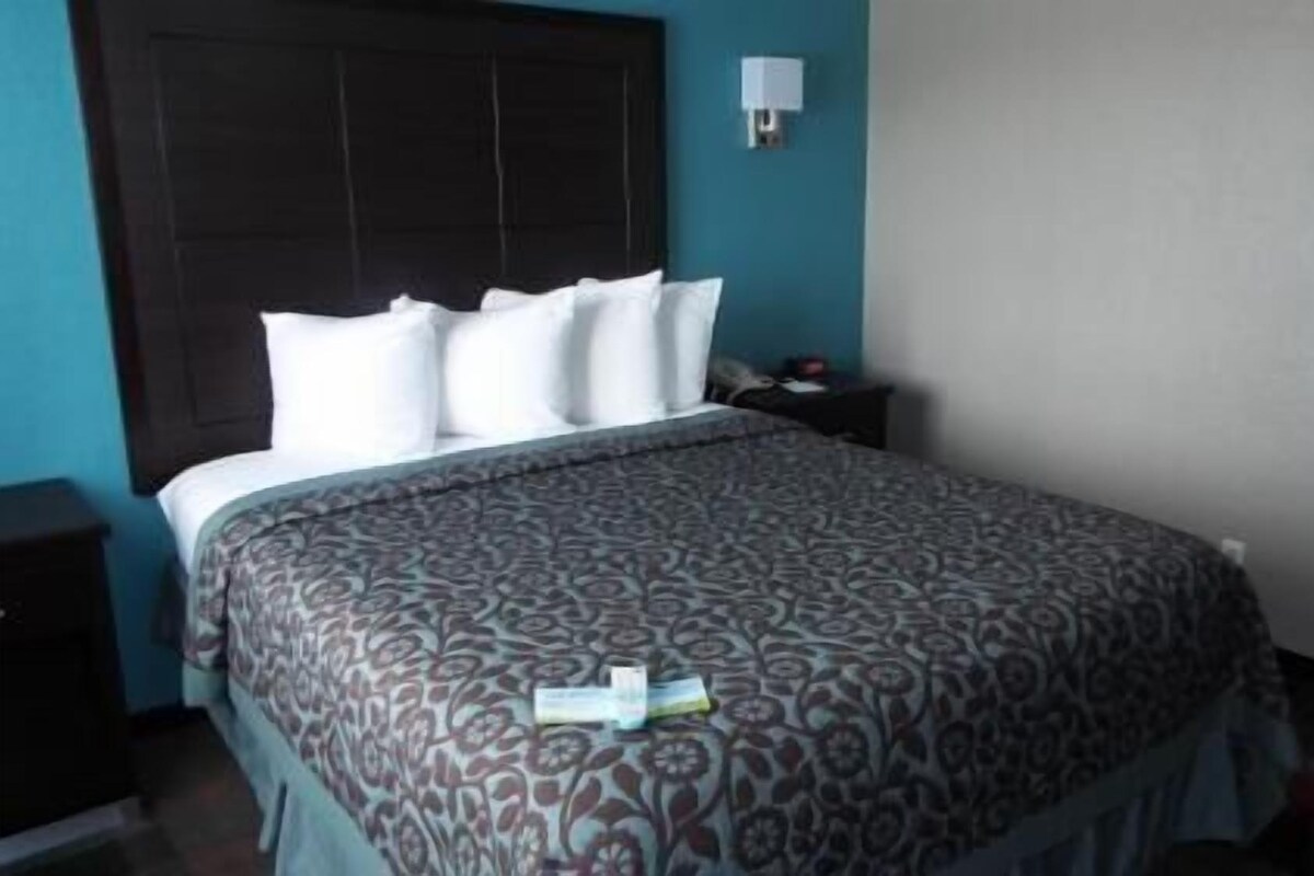 A bedroom with a bed, a nightstand, a wall-mounted lamp, and a door.