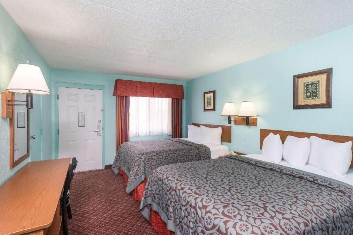 A hotel room with two beds, a desk, a chair, a door, and two wall-mounted lamps.