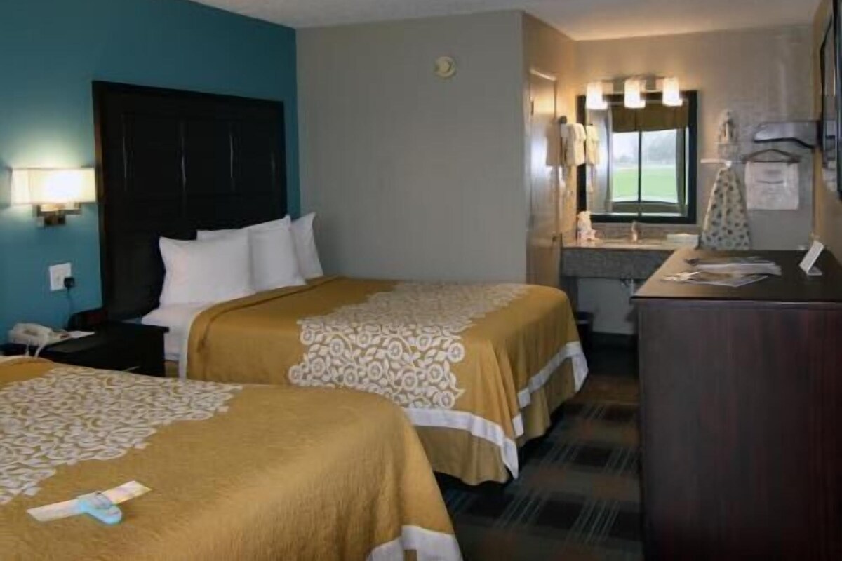 A hotel room with two beds, a desk, a mirror, and a window.