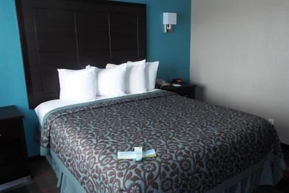 A bedroom with a bed, a nightstand, a wall-mounted lamp, and a door.