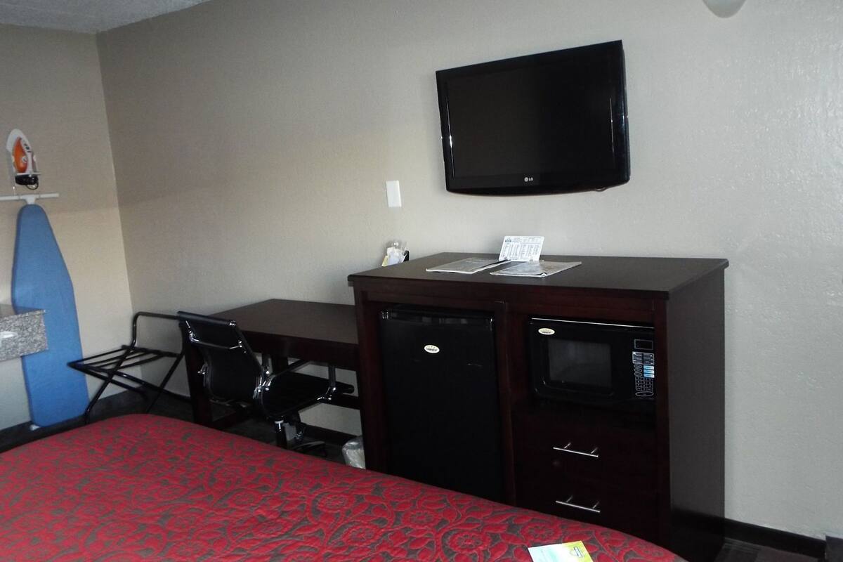 A hotel room with a bed, a desk, a chair, a microwave, and a flat-screen TV.