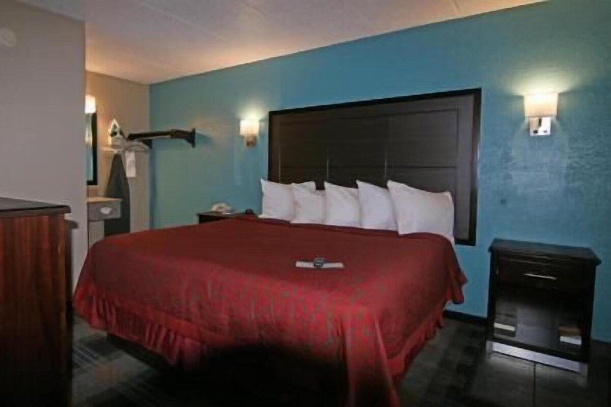 A hotel room with a large bed, a nightstand, a dresser, and a wall-mounted lamp.