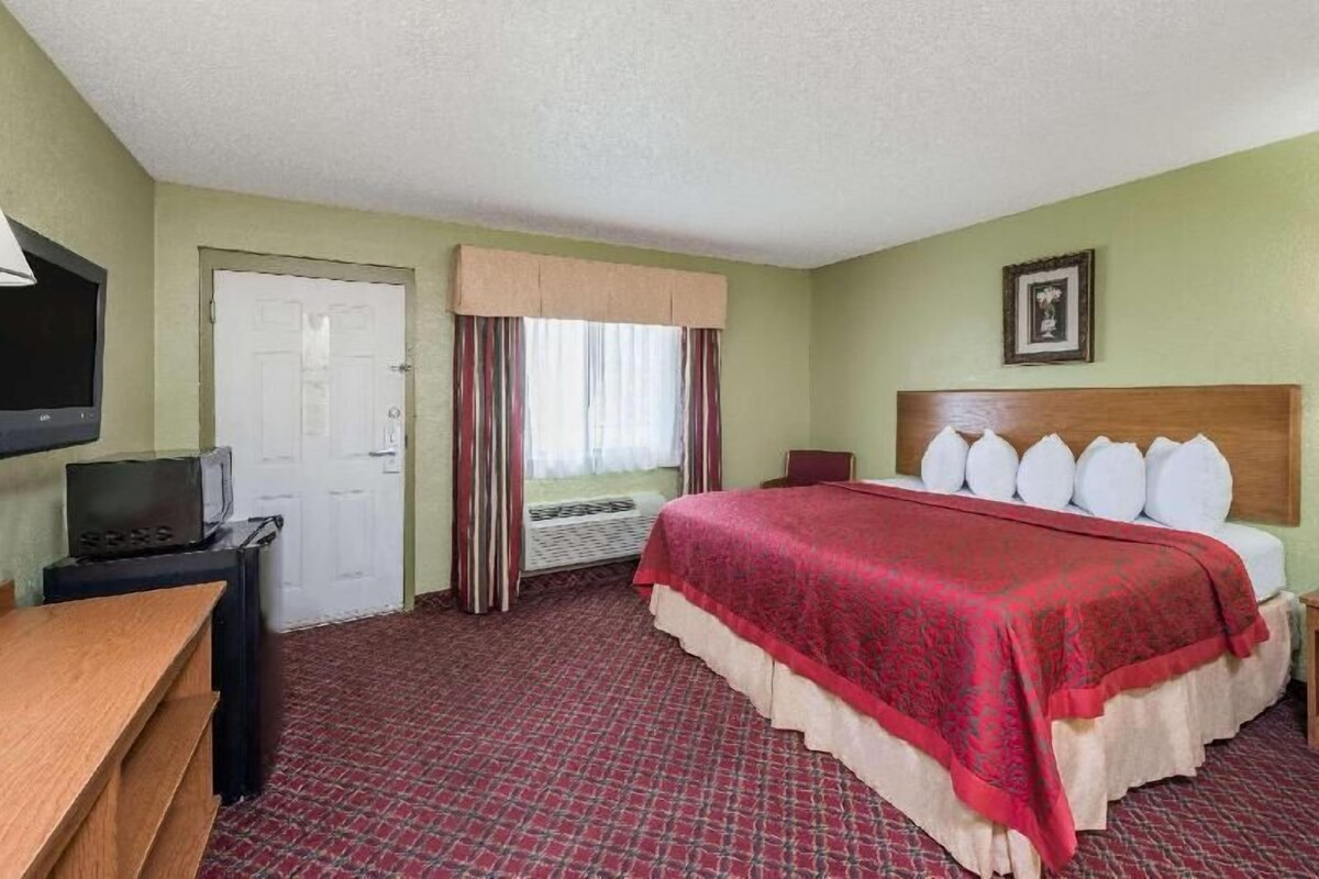 A hotel room with a bed, a desk, a television, a door, and a window with curtains.