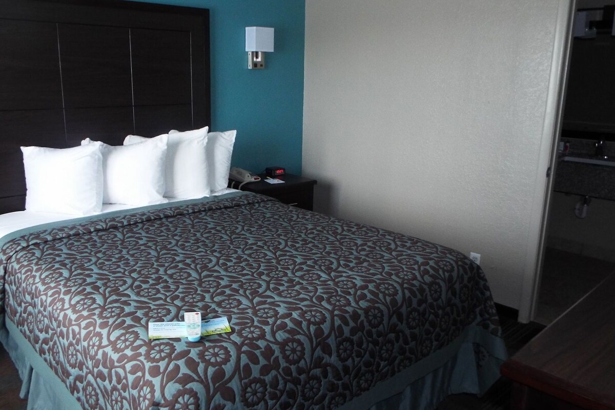 A hotel room with a bed, a nightstand, a bedside table, and a wall-mounted lamp.