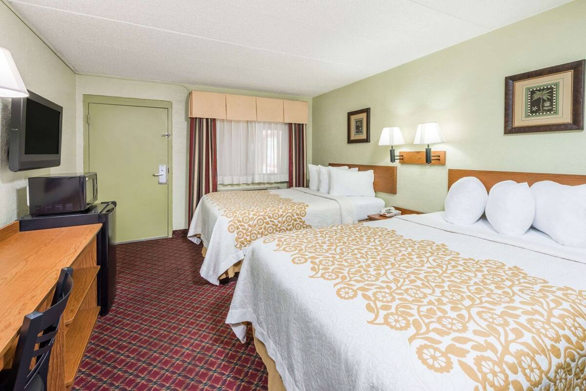 A hotel room with two beds, a desk, a television, and a door.