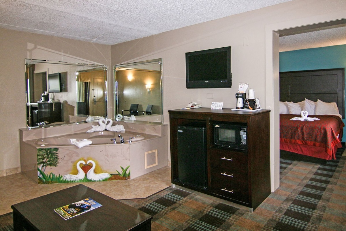 A hotel room with a large bathroom vanity, a flat-screen TV, a bed with a red bedspread, and a coffee machine.