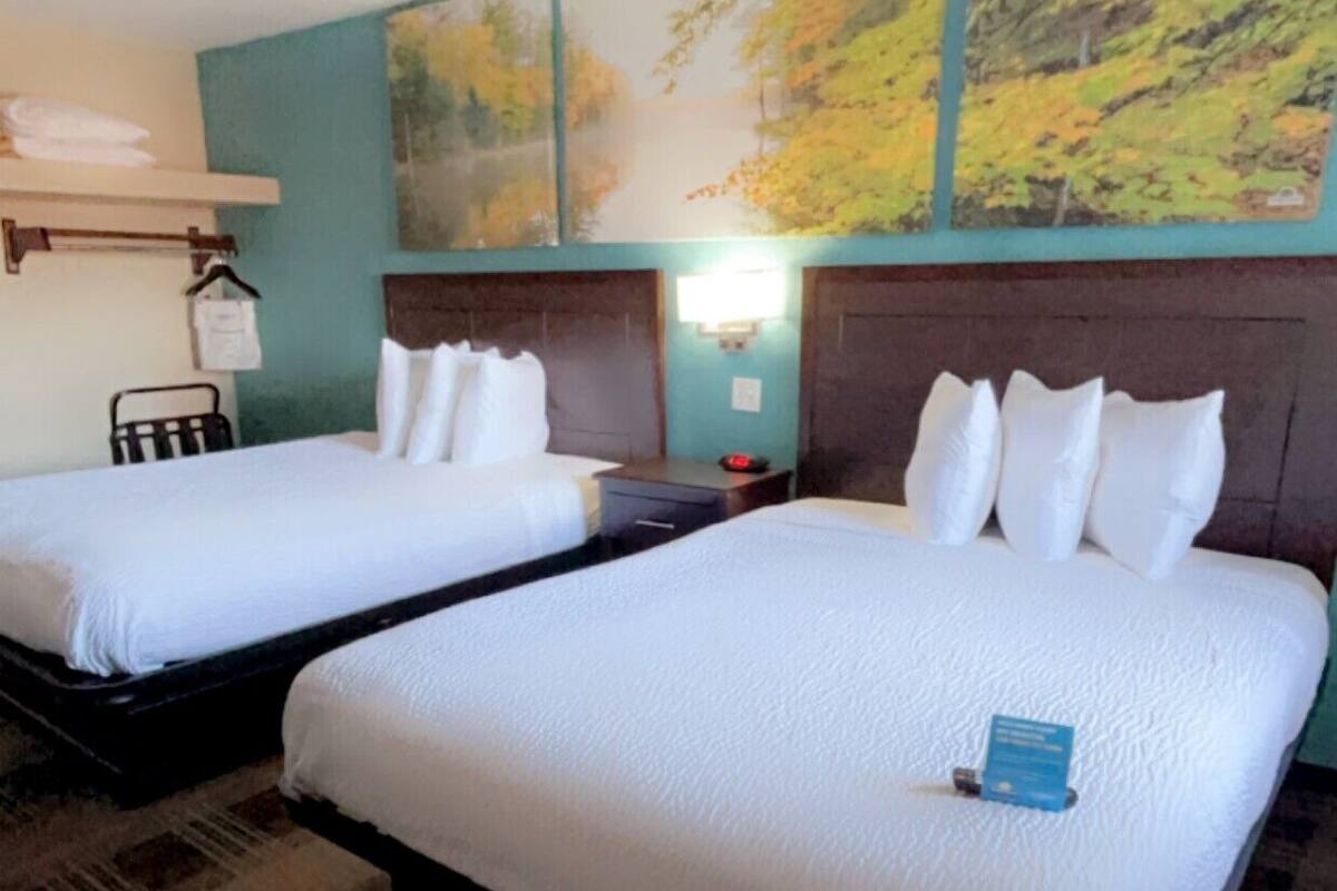 A hotel room with two single beds, a nightstand, a lamp, and a painting on the wall.