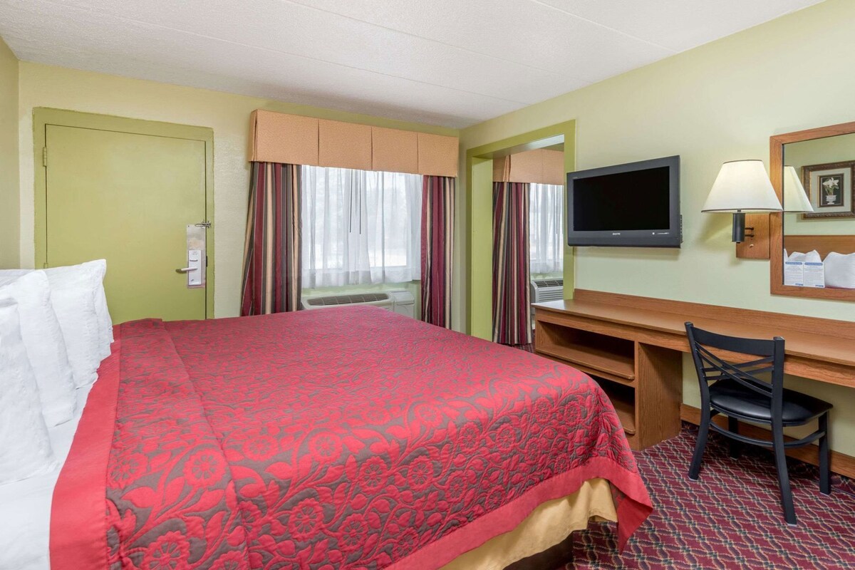 A hotel room with a bed, a desk, a chair, a television, and a mirror.