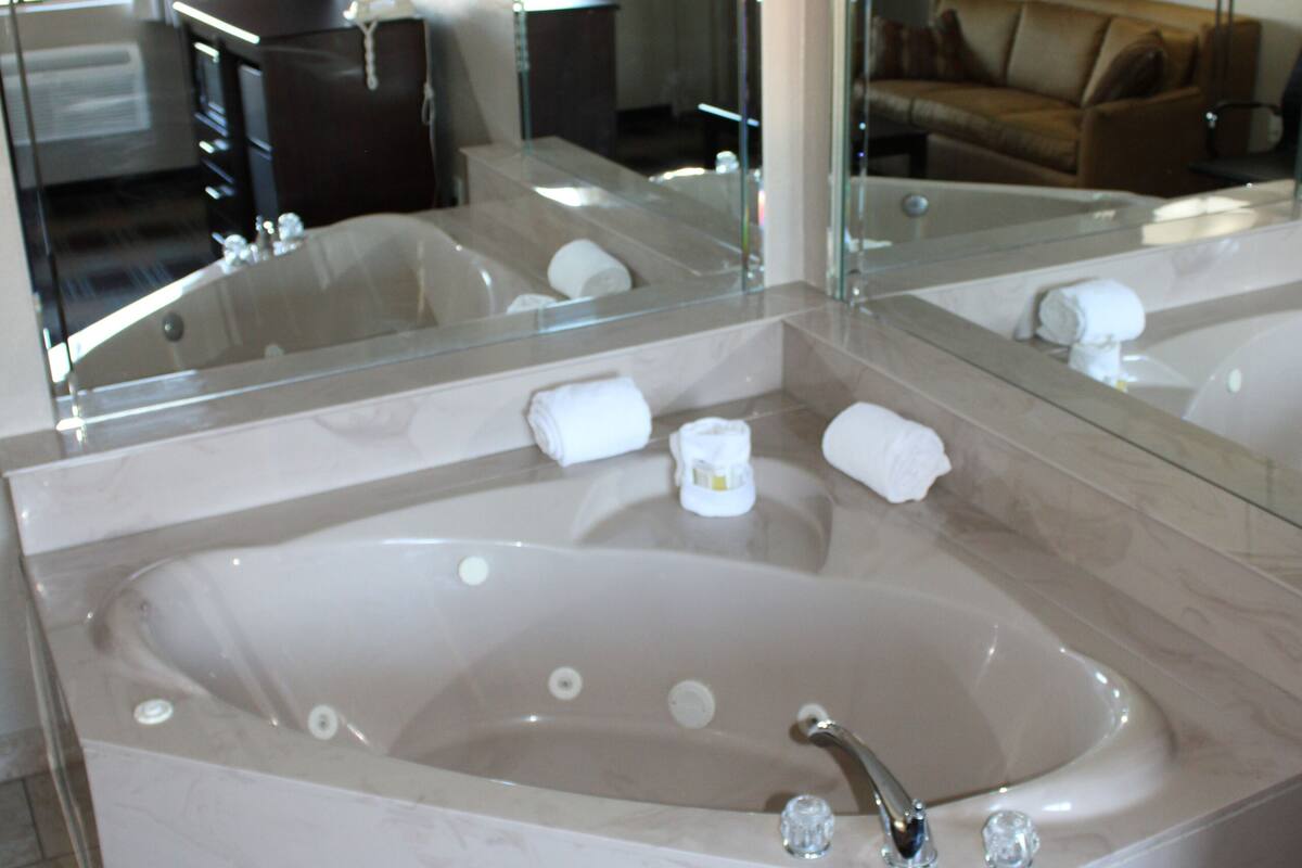 A large, freestanding bathtub with a glass enclosure and a large mirror above it.