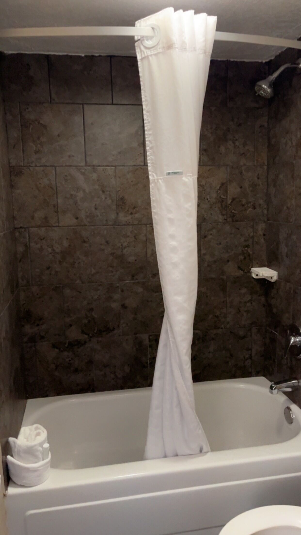 A bathtub with a white shower curtain, a white towel, and a white soap dispenser.