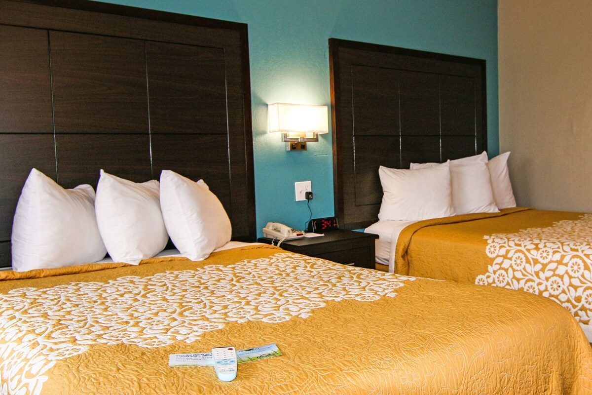 A hotel room with two beds, a nightstand, a lamp, and a digital clock.