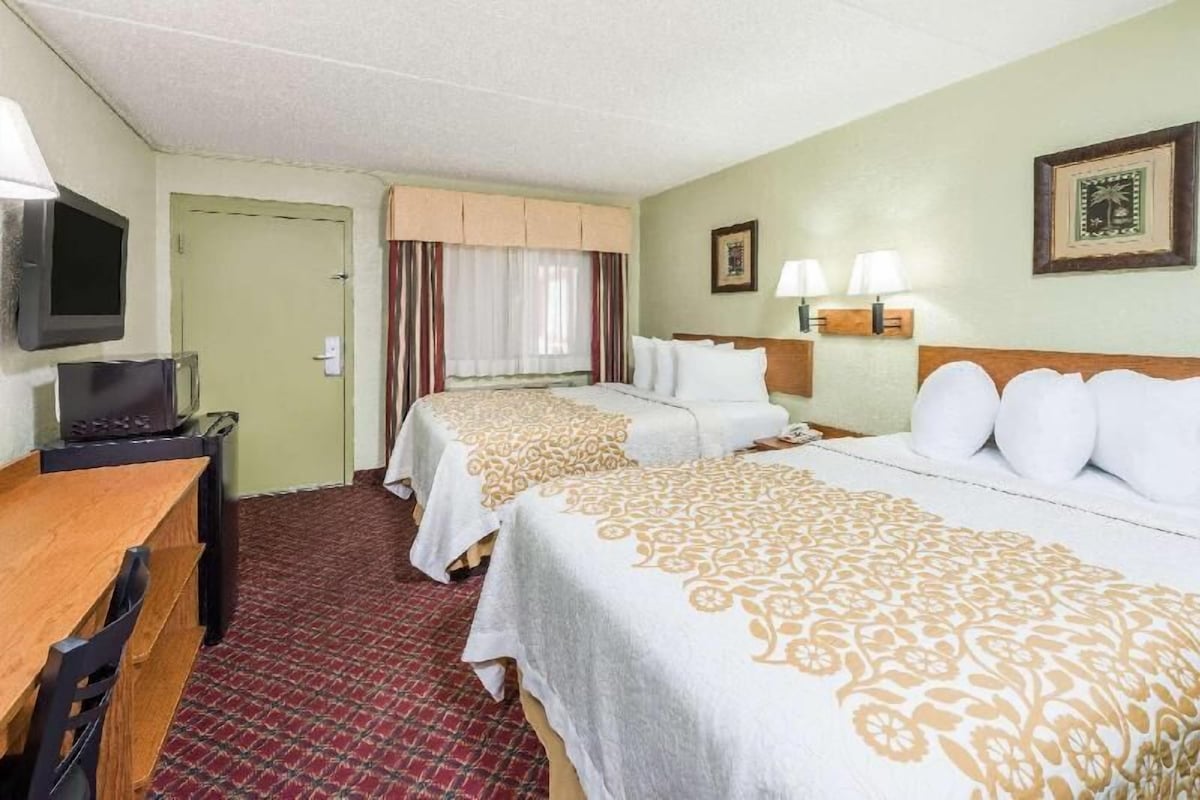 A hotel room with two beds, a desk, a television, and a door.