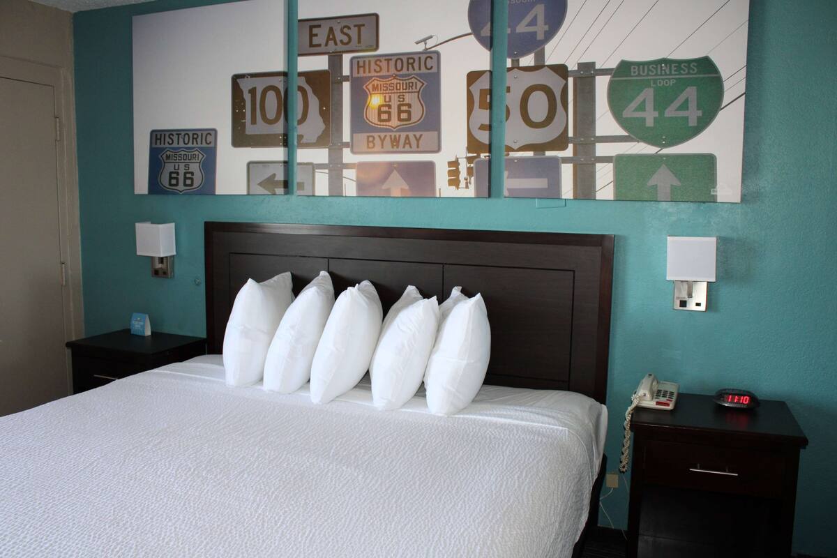 A hotel room with a bed, a nightstand, a wall clock, and a wall-mounted telephone.