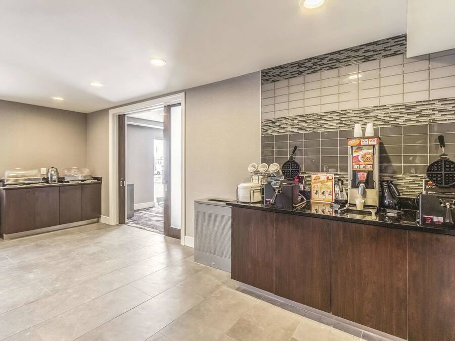 A modern hotel lobby with a self-service breakfast area, including a waffle maker and coffee machine.