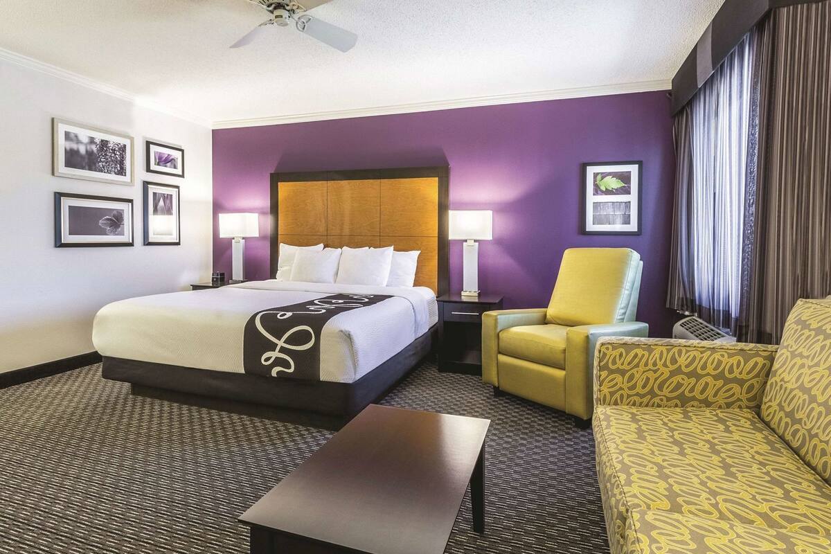 Ein Hotelzimmer mit einem Bett, einer Couch, einem Sessel, einem Tisch, einem Deckenventilator und Wandlampen.