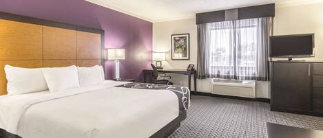 A hotel room with a large bed, a desk, a chair, a television, and a ceiling fan.