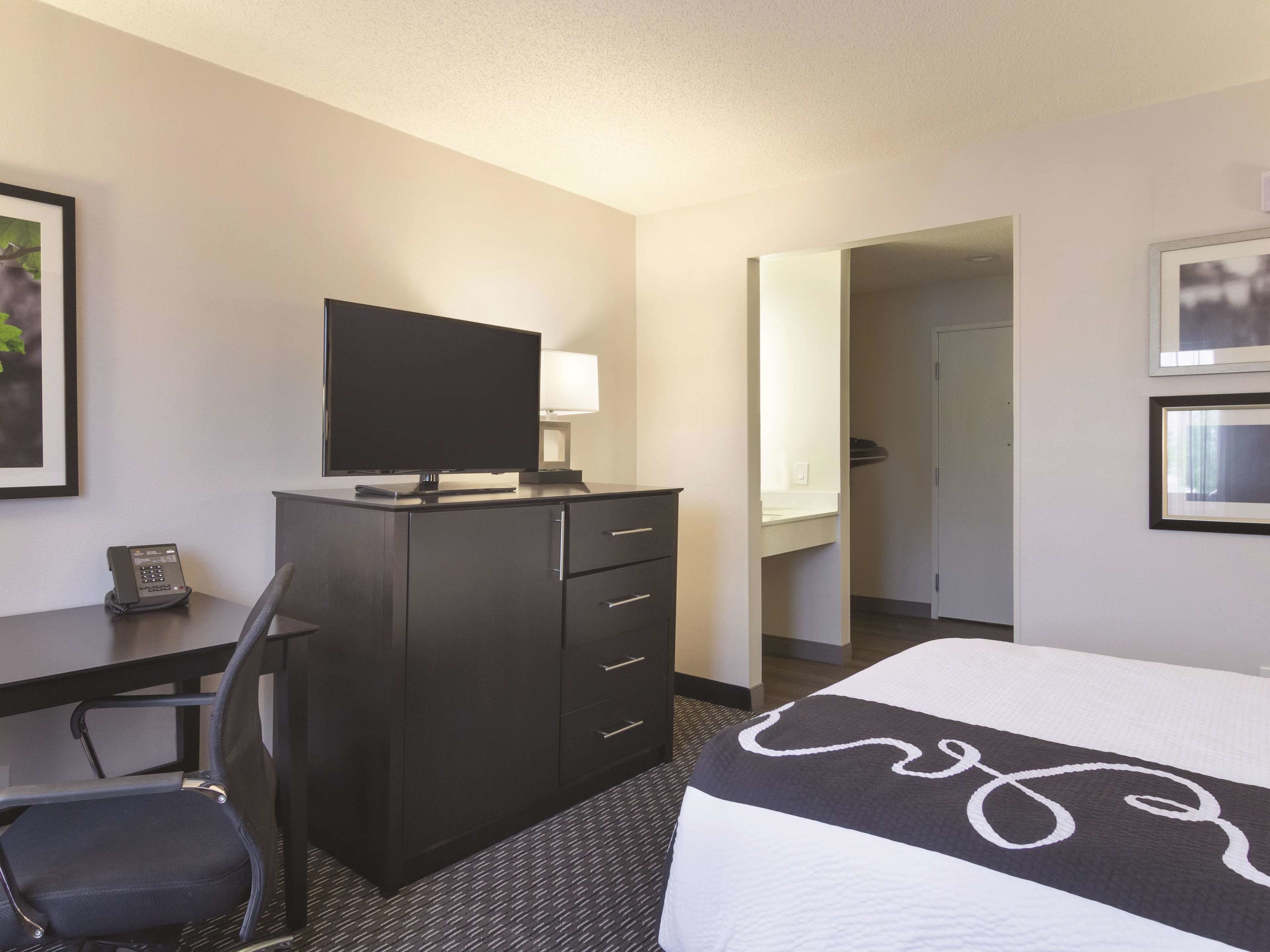 Quarto de hotel com cama, escrivaninha, televisão de tela plana, cadeira, cômoda e espelho.