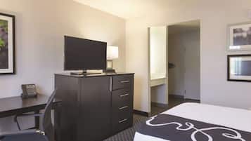 A hotel room with a bed, a desk with a flat-screen TV, a chair, a dresser, and a mirror.
