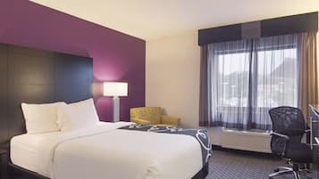 A hotel room with a large bed, a desk, a chair, a lamp, and a window with curtains.