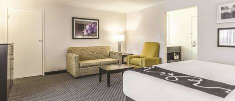A hotel room with a bed, a sofa, a chair, a desk, and a ceiling fan.
