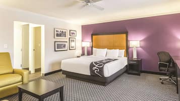 A hotel room with a bed, a desk, a chair, a small table, and a ceiling fan.