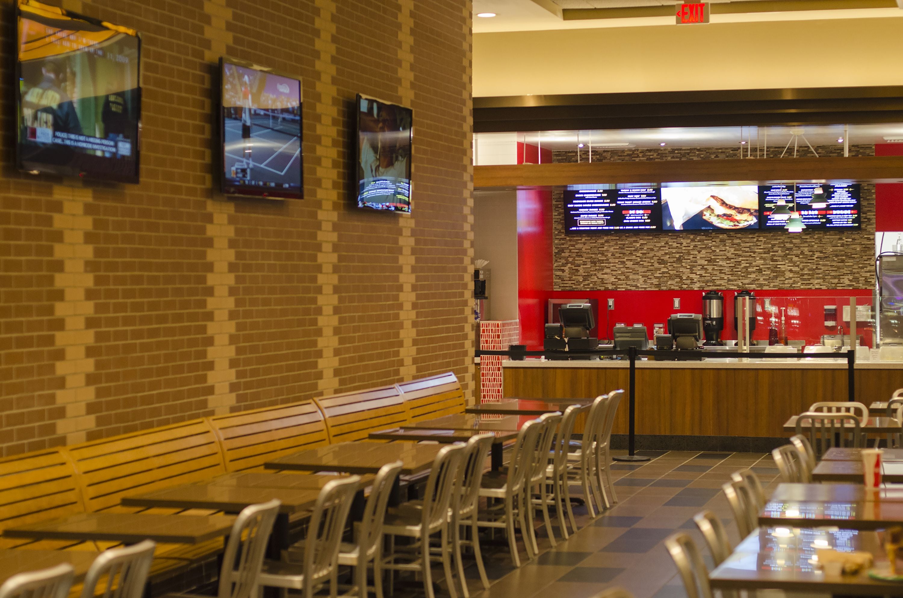 A restaurant with brick walls, multiple screens displaying menus, and a counter with a coffee machine.