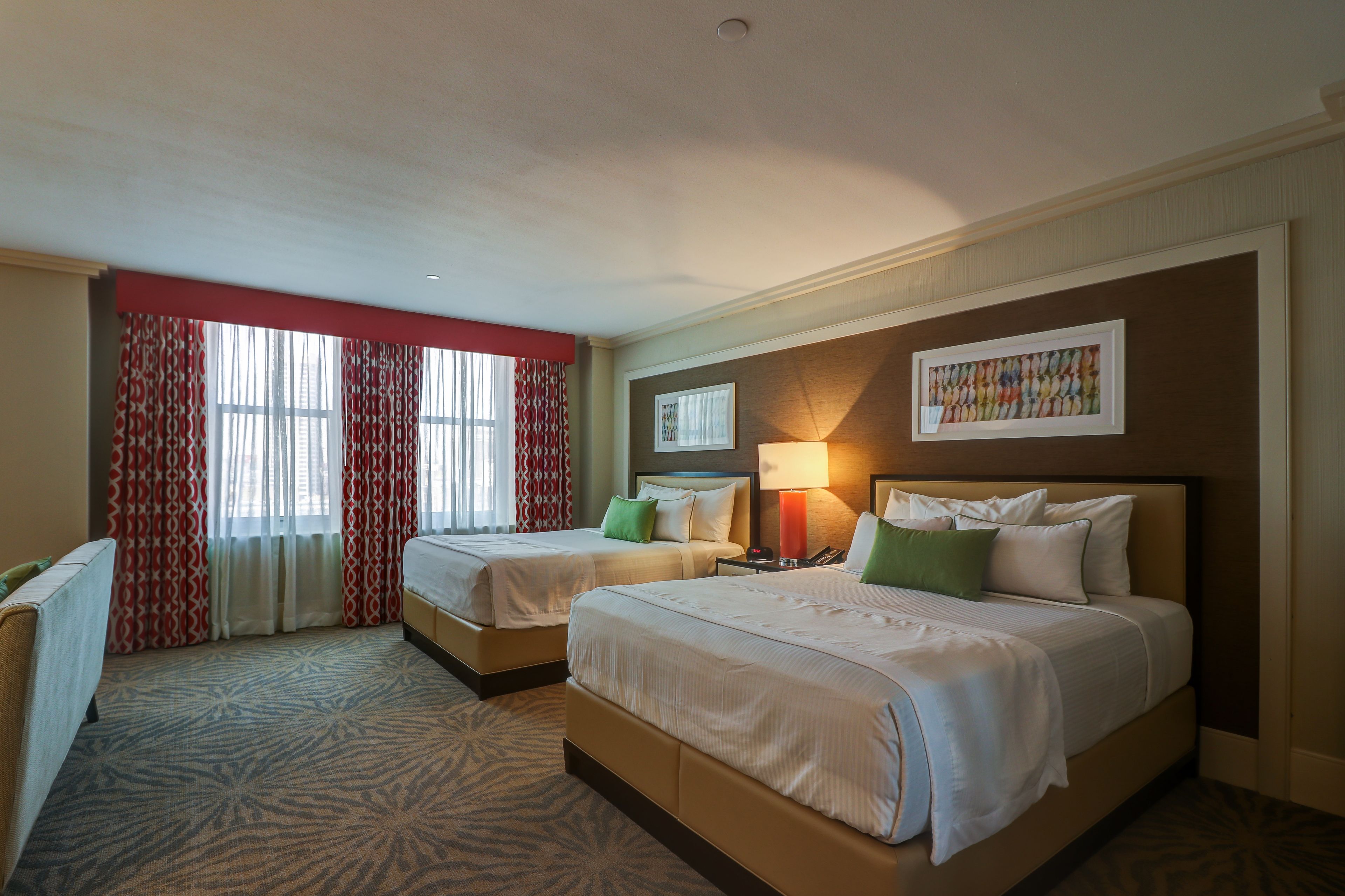 A hotel room with two beds, a desk, a lamp, and a window with curtains.