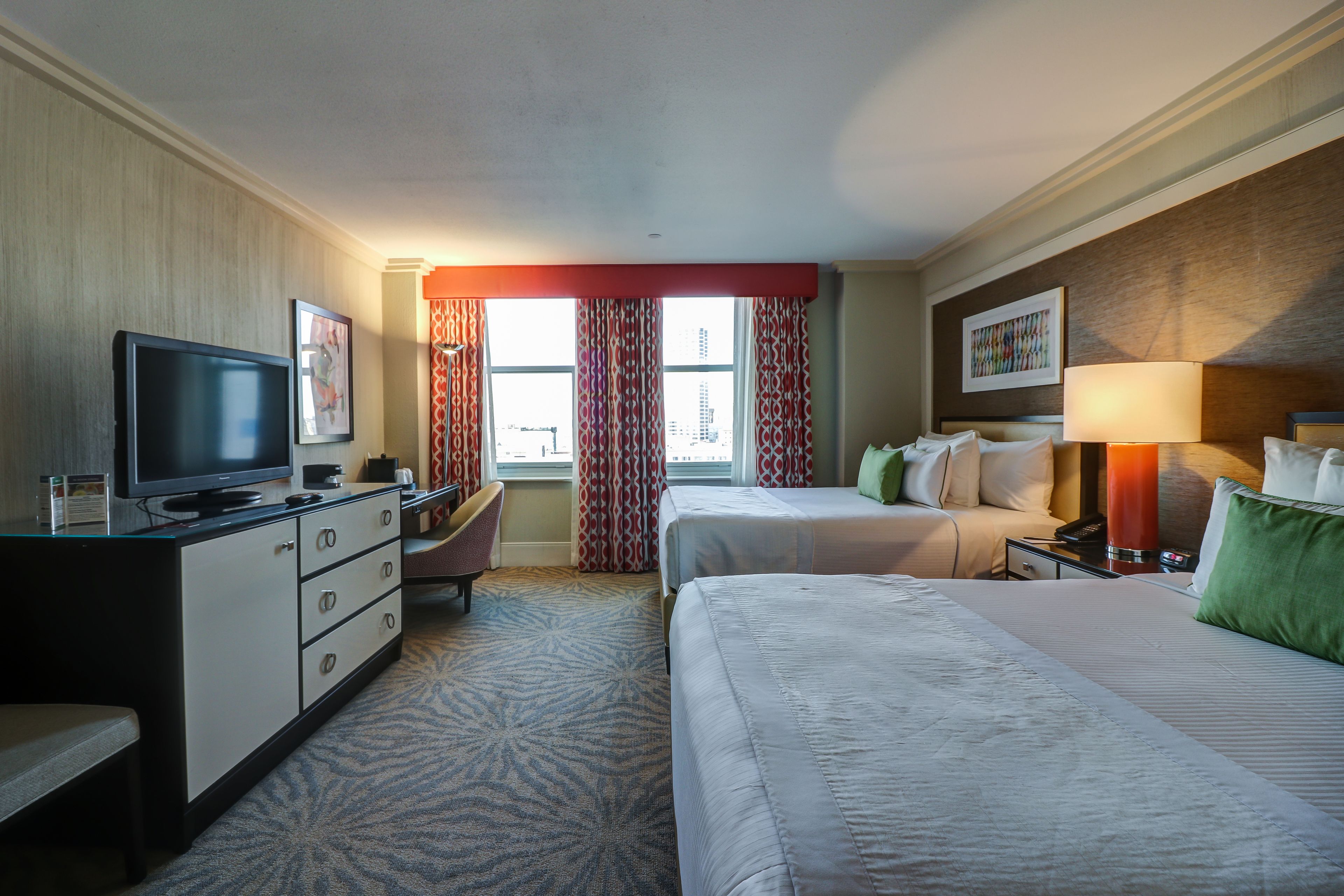 A hotel room with a bed, a desk with a television, a chair, and a window with curtains.