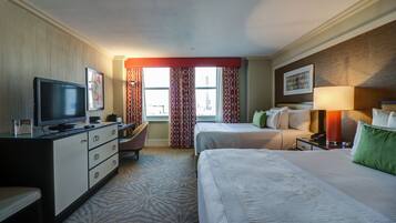 A hotel room with a bed, a desk with a television, a chair, and a window with curtains.