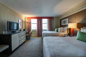 Habitación de hotel con cama, escritorio con televisor, silla y ventana con cortinas.