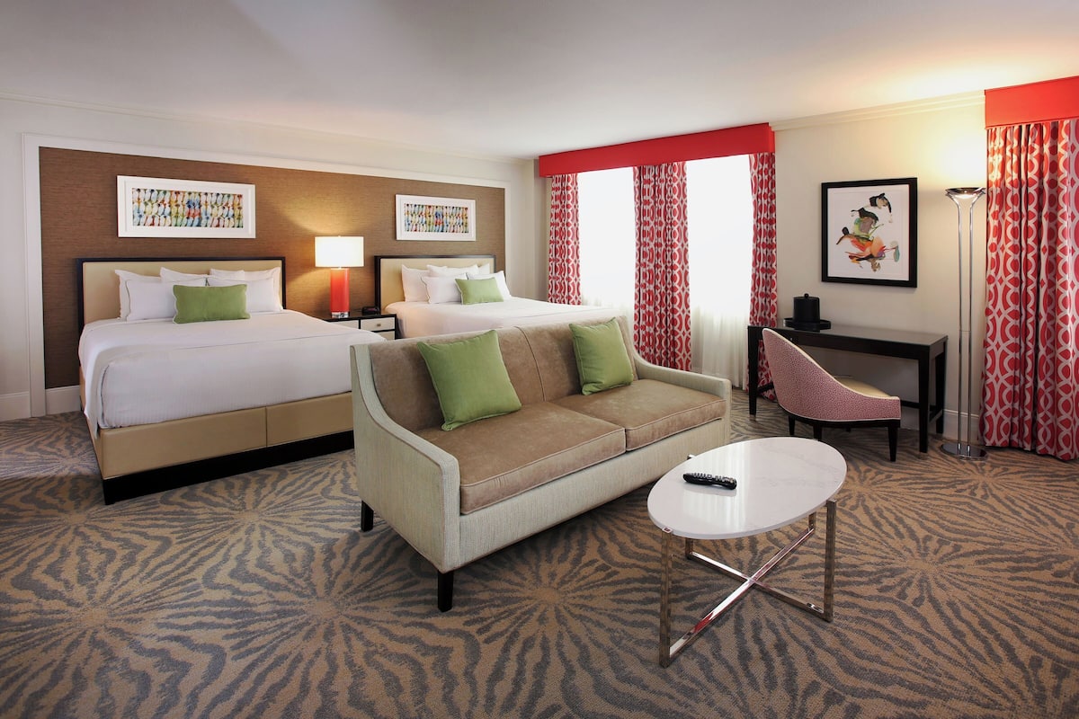 A hotel room with two beds, a sofa, a small table, and a desk.
