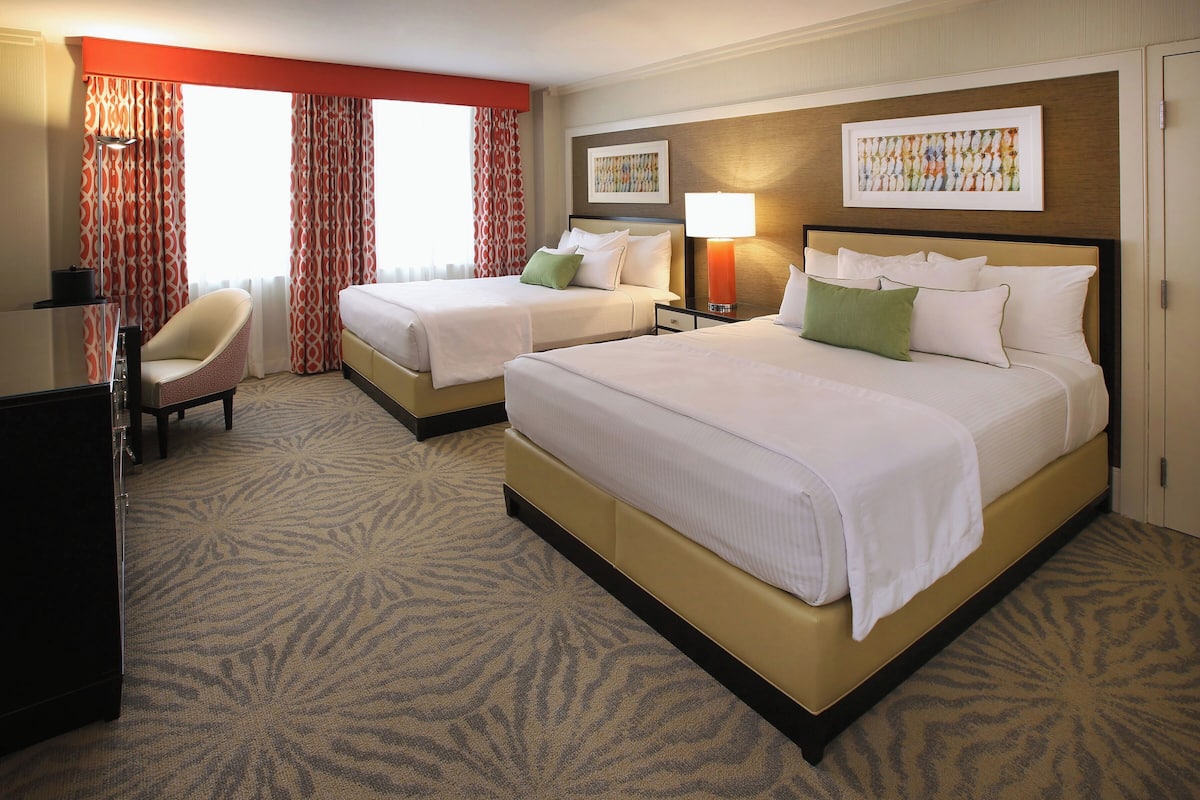 A hotel room with two beds, a desk, a chair, and a carpeted floor.