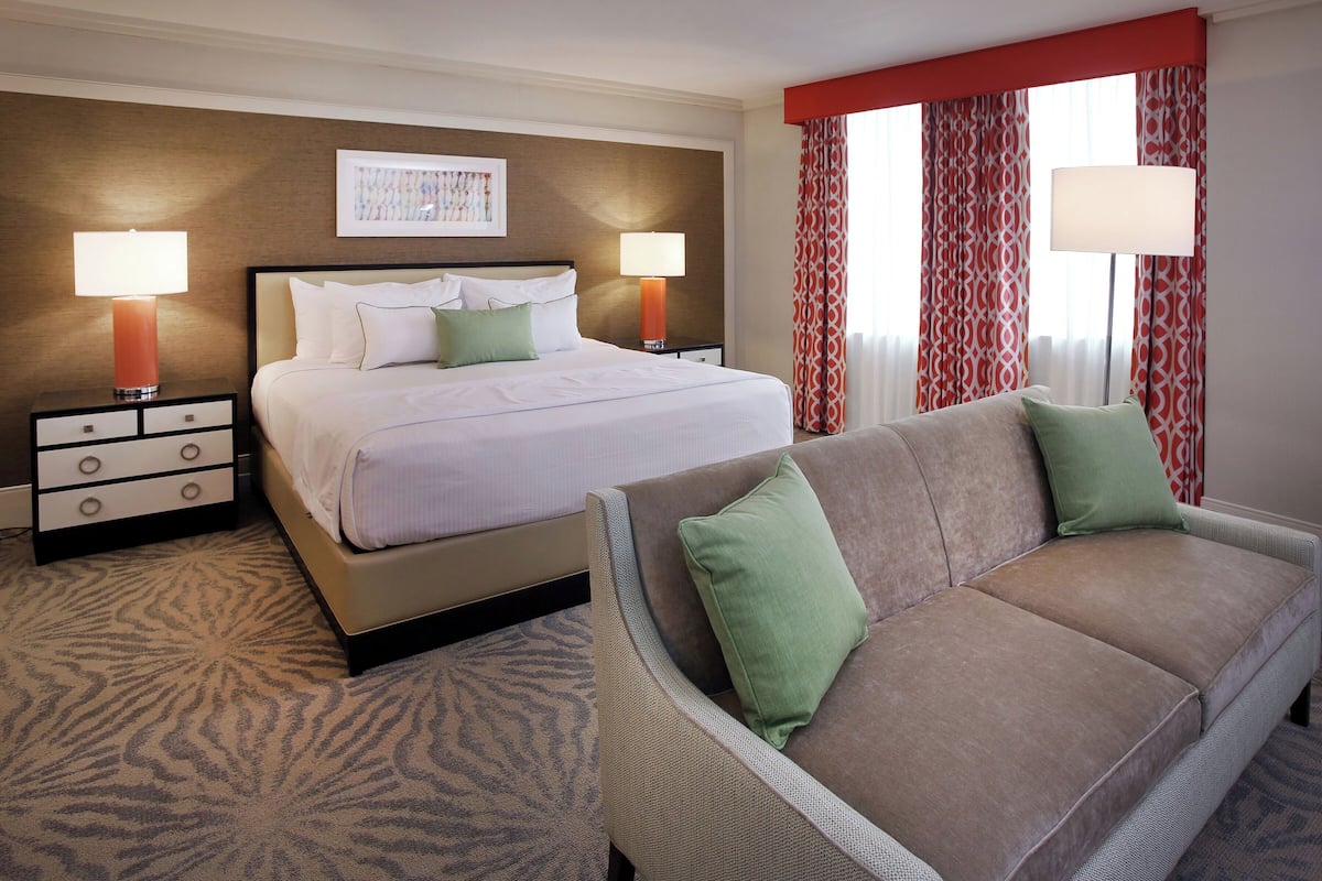 A hotel room with a bed, two bedside tables with lamps, a sofa, and a patterned carpet.