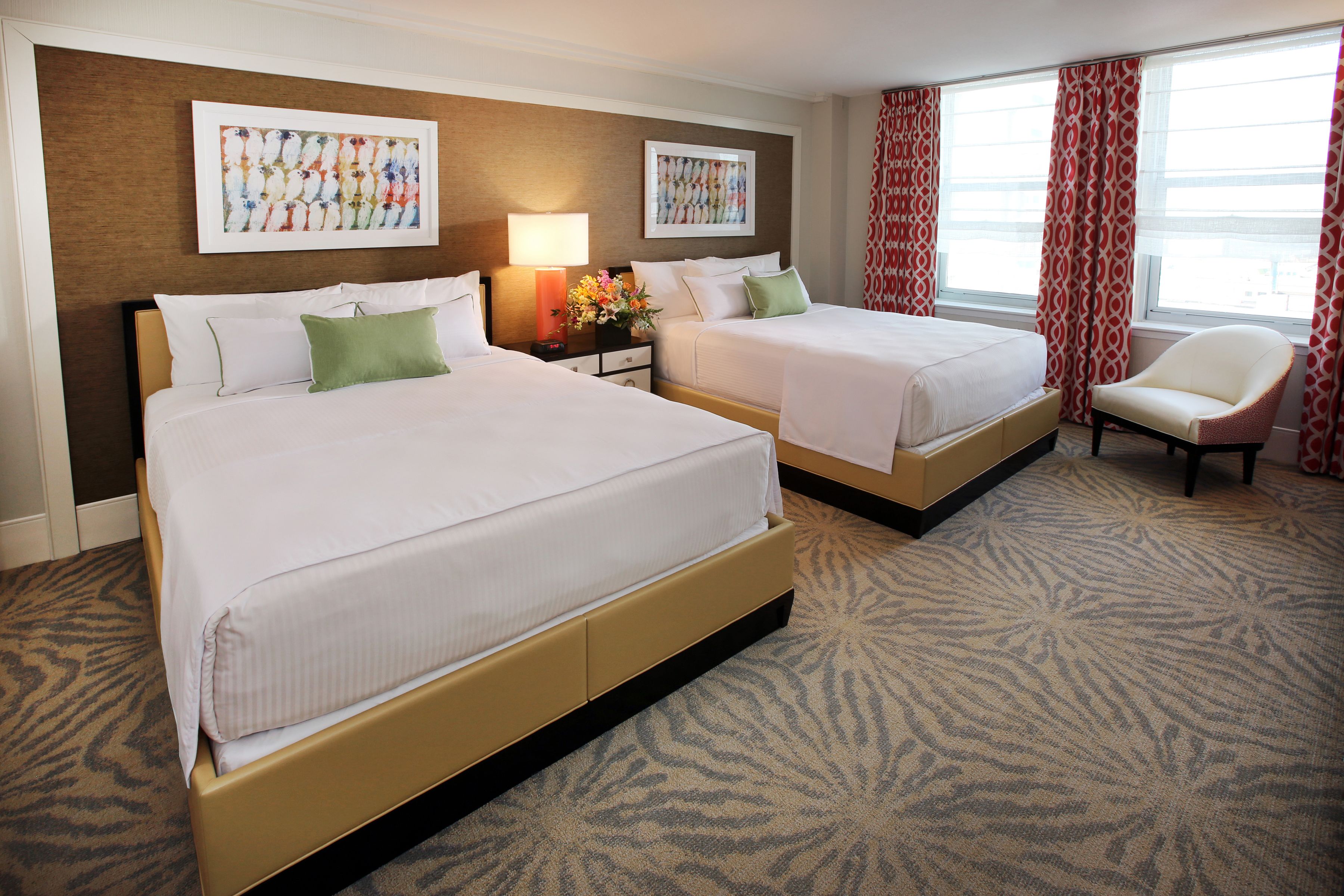A hotel room with two beds, a nightstand with a lamp, a chair, and artwork on the walls.