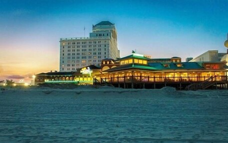 A beachfront hotel with a prominent building in the background and a well-lit structure in the foreground.