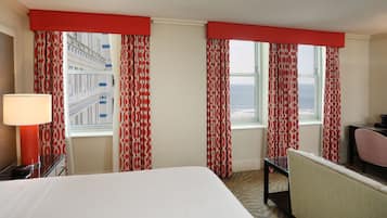 Une chambre d’hôtel avec un lit, un bureau, une chaise et une fenêtre avec des rideaux.