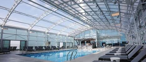 An indoor swimming pool with a glass ceiling, lounge chairs, and a clear view of the sky.