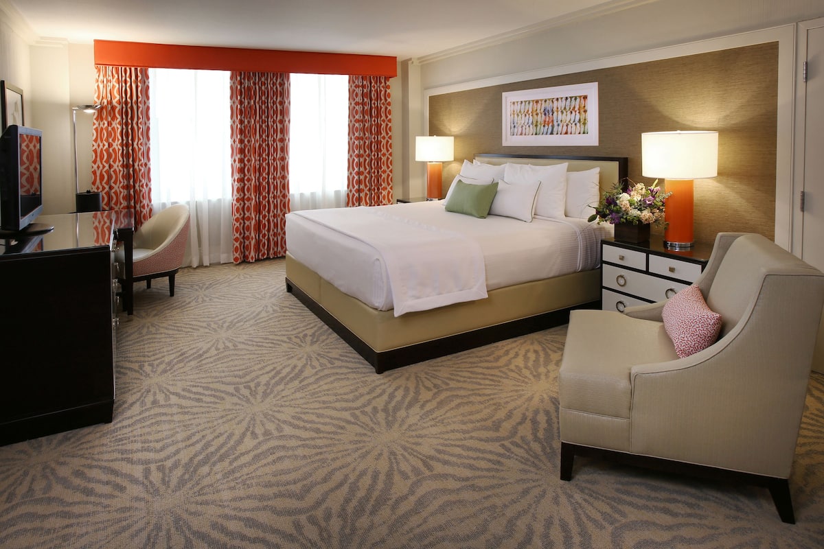 A hotel room with a large bed, two bedside tables with lamps, a desk with a chair, and a patterned carpet.